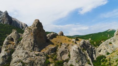 Yeşil dağların ve mavi gökyüzünün arka planındaki kayalıkların üst görüntüsü. Vuruldu. Kaya kütleli güzel dağ manzarası ve gökyüzünün arka planında yeşil çimenler
