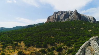 Gökyüzünün arka planındaki yeşil dağın tepesindeki dik kayalık yamaçların üst manzarası. Vuruldu. Resimli yeşil dağların güzel kayalık tepesi