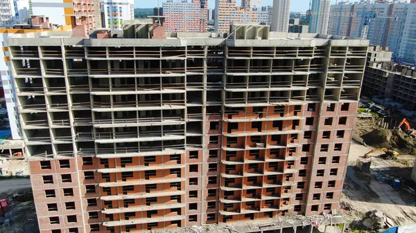 Вид сверху на стройплощадку современного многоэтажного здания. Движение. Кирпичный фасад многоэтажного строящегося здания в современном благоустроенном районе — стоковое фото