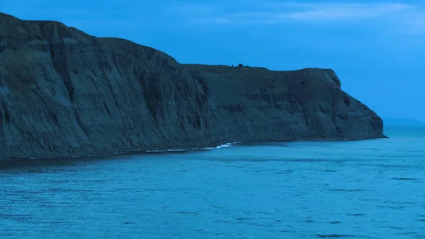 Aerial view of the sea near the coast. Shot. Top view of the high cliffs near the sea. A raging sea breaking waves on rocks