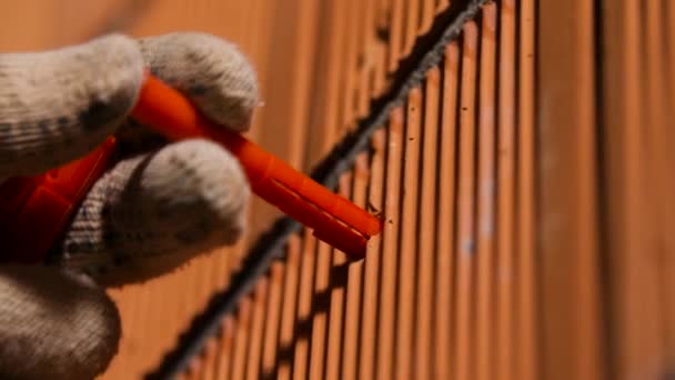 Le menuisier insère une cheville. Images d'archives. Gros plan de l'homme en gants insérant une cheville dans un trou dans un mur de briques. Détails de construction pour les attaches — Video