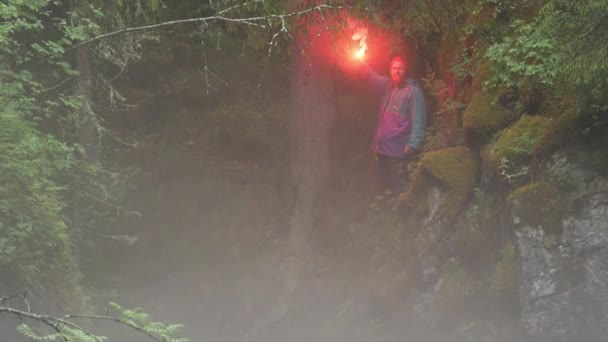 Red signal flare in a hand of young scared man hiker lost in dense forest in the evening. Stock footage. Traveler making a signal to be found. — 비디오