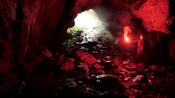 La silhouette di un uomo con un segnale rosso che brucia all'interno di un'entrata di una caverna. Filmati delle scorte. Alla scoperta di pericolosi sentieri sotterranei . — Video Stock