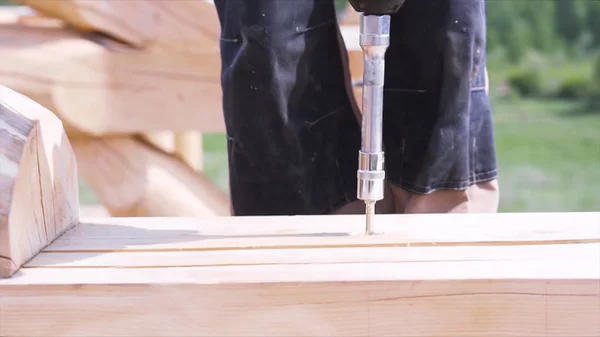 Close up of carpenter hands using professional screwdriver outdoors at construction site. Clip. Man working with professional equipment while wooden house building.