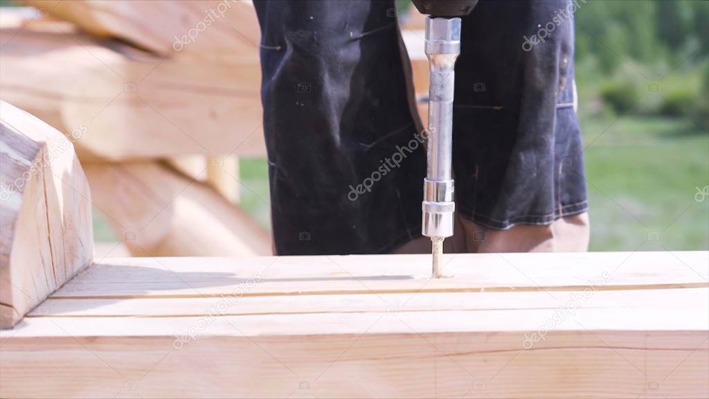 Close up of carpenter hands using professional screwdriver outdoors at construction site. Clip. Man working with professional equipment while wooden house building.