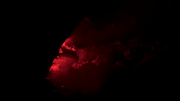 Silhouette d'homme dans une crypte souterraine abandonnée avec une fusée éclairante rouge brûlante. Images d'archives. Homme accroupi devant un trou de grotte dans l'obscurité totale . — Video