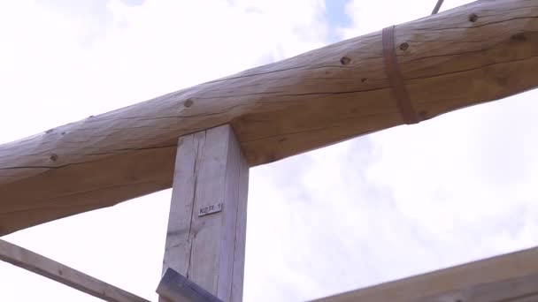 Das hölzerne Gerüst des umweltfreundlichen Neubaus vor wolkenverhangenem Himmel. Clip. Blick von unten auf einen Baumstamm, der auf der Holzkonstruktion installiert wird. — Stockvideo