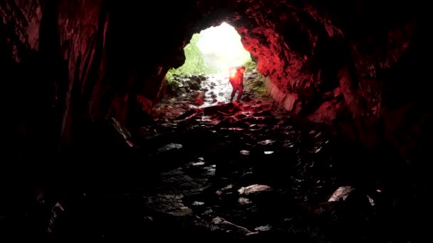 La silhouette di un uomo con un segnale rosso che brucia all'interno di un'entrata di una caverna. Filmati delle scorte. Alla scoperta di pericolosi sentieri sotterranei . — Video Stock