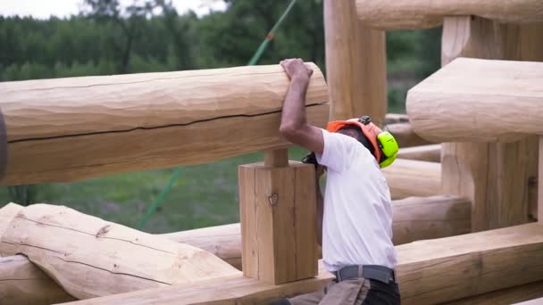 在安装新的木制建筑墙体时，木匠戴着防护耳机和头盔的后视镜。 剪断。 建筑工地的工人. — 图库视频影像