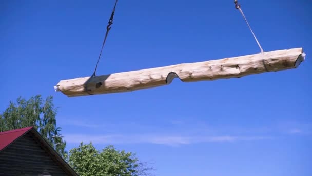 Kran hebt Holzbalken auf blauem Himmelshintergrund. Clip. Element des neuen umweltfreundlichen Hauses im ländlichen Raum, Zimmereiarbeiten Konzept. — Stockvideo