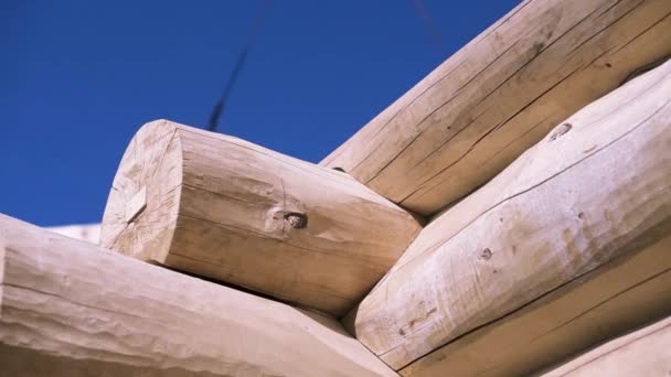 Detalle de vigas, la esquina de la casa de madera sin terminar sobre fondo azul cielo nublado, vista inferior. Clip. Brazo de grúa moviéndose detrás del marco del edificio de madera . — Vídeos de Stock