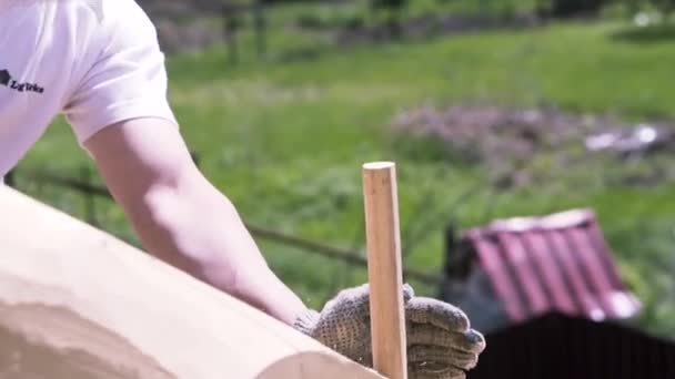 Close-up van een timmerman hameren de houten pin in het logboek, details van nieuwe onvoltooide gebouw. Een knip. Mannelijke werknemer die het houten huisje bouwt. — Stockvideo