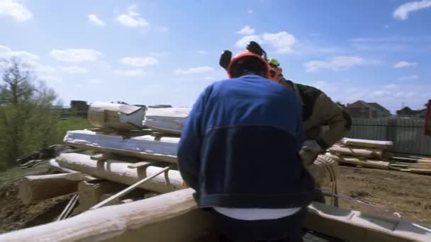 Rear view of carpenters make markings on a wooden log at the construction site with the crane machine on the background. Clip. Process of new wooden house building. — Stock Footage Rear view of carpenters make markings on a wooden log at the construction site with the crane machine on the background. Clip. Process of new wooden house building. Royalty Free Stock Video