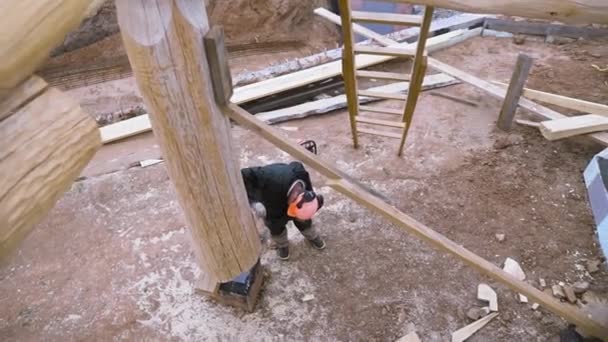 Bovenaanzicht van timmerman het bouwen van nieuwe houten ecologische huis of huisje op het platteland. Een knip. Mannelijke werknemer in uniform en beschermhelm op de bouwplaats. — Stockvideo