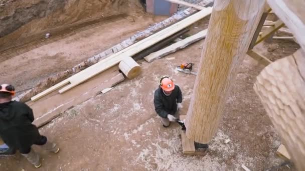Κάτοψη ενός αρσενικού ξυλουργού που χαλαρώνει την ένταση του γρύλου για να υποστηρίξει το στοιχείο του ξύλινου τοίχου στο εργοτάξιο. Κλιπ. Ξύλινο κτίριο χωρίς φινίρισμα, εργασία σε εξωτερικούς χώρους. — Αρχείο Βίντεο