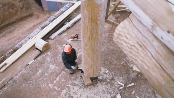Зверху чоловік, тесляр, розслаблює натяг валета, щоб підтримувати дерев "яний елемент стіни на будівельному майданчику. Кліп. Незакінчена дерев "яна будівля.. — стокове відео