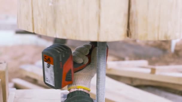 O trabalhador trabalha com uma chave de fenda, no fundo de vigas de madeira, obras de carpintaria no canteiro de obras. Clipe. Close-up de mão masculina desaparafusar parafuso de metal fora de madeira tronco redondo . — Vídeo de Stock