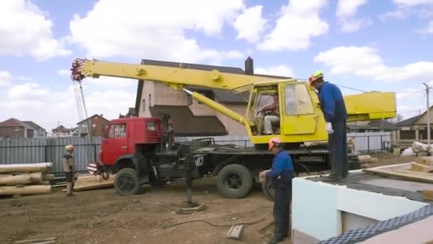 Heavy machinery and the crew of male carpenters at the construction site. Clip. Rear view of workers and machinery on blue cloudy sky background. — Stock Video