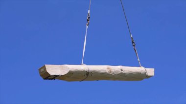 Yeni evin ahşap elementinin vinç ve inşaat halatı yardımıyla yerleştirilmesi. Şarjör. Günlük kaydı taşınıyor ve kaldırılıyor mavi gökyüzü arkaplanı, alt görünüm.