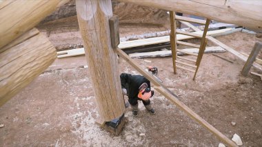 Marangoz manzaralı yeni ahşap ekoloji evi ya da kırsal alanda bir kulübe inşa ediyor. Şarjör. İnşaat alanında üniformalı ve kasklı bir erkek işçi..