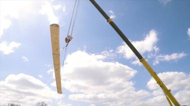 Mavi bulutlu arka planda büyük ahşap kiriş taşıyan vincin alt görüntüsü. Şarjör. Tamamlanmamış evin ahşap çerçevesinin ayrıntıları.