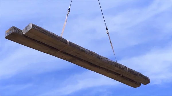 Zwei Holzbalken, die vom Kran auf blauem wolkenverhangenem Himmel transportiert werden. Clip. Blick von unten auf Baumstämme in der Luft. — Stockfoto