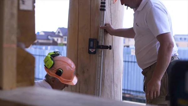 Sluiten van kleine hoogte liggend op een houten balk. Een knip. Twee timmerlieden met professionele uitrusting op de bouwplaats. — Stockfoto