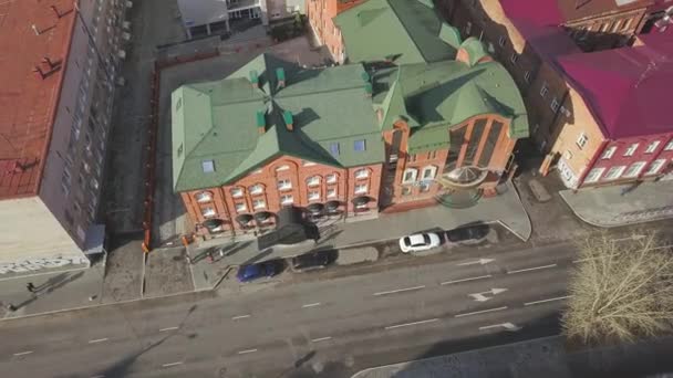 Luftaufnahme von Gebäuden und der Stadtstraße mit fahrenden Autos an einem sonnigen Herbsttag. Clip. Blick von oben auf das rote Backsteinschulgebäude mit begrüntem Dach, Architekturkonzept. — Stockvideo