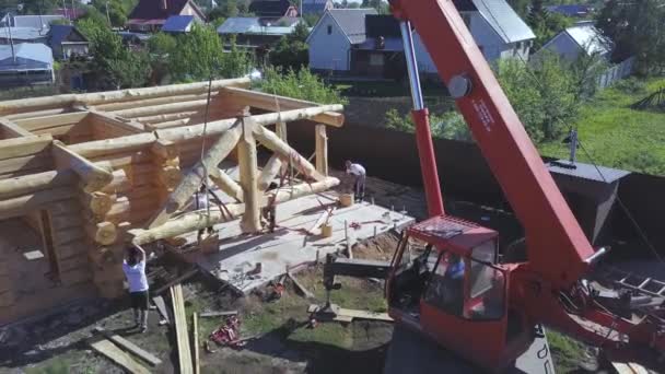 Aerial of the timber frame construction with a professional crane machine on a summer sunny day. Clip. Flying above the village and unfinished wooden building. — Stock Video