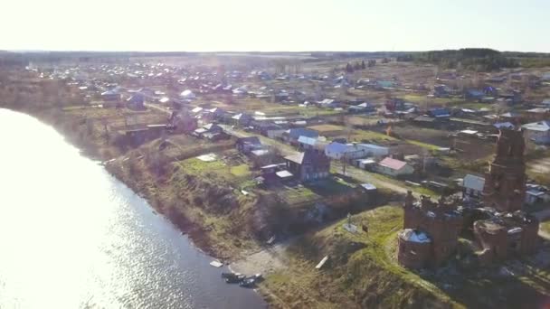 Flygfoto av förstörd kyrka nära sjön och liten stad på solnedgången ljus himmel bakgrund. Klipp. Flyg ovanför byn och grön äng. — Stockvideo