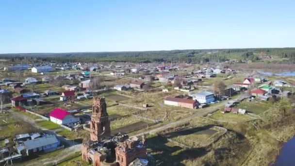 Övergiven raserad kyrka byggd vid den blå flodstranden, höstlandskapet. Klipp. Flyg över byn med små hus och grön äng. — Stockvideo