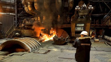 Metalürji fabrikasındaki dev fırına bakan iki mühendisin arka görüntüsü, ağır sanayi konsepti. Stok görüntüleri. Fabrikanın içinde iki erkek işçi var..
