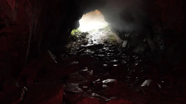 Uitzicht vanuit een grot met rotsachtig pad en daglicht bij de ingang. Voorraadbeelden. Onbekende ondergrondse tunnel, gevaarlijk reisconcept. — Stockfoto