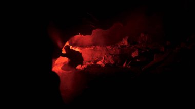 Man silhouette in an underground abandoned crypt with burning red signal flare. Stock footage. Man squatting in front of a cave hole in complete darkness. clipart