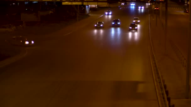 Pemandangan malam dari jalan beton di bawah lampu jalan menyala dengan mobil mengemudi. Rekaman saham. Larut malam lalu lintas di jalan kota dengan kendaraan bergerak . — Stok Video