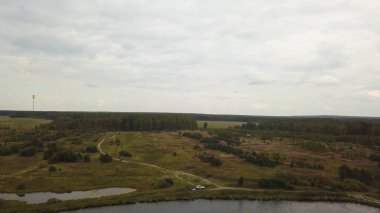 Geniş nehrin yanında yeşil ağaçlar ve bulutlu gökyüzü arka planında çayırlar olan yaz kırsal arazisi, hava manzarası. Stok görüntüleri. Kırsal kesimde piknik manzarası, nehir kıyısında park edilmiş bir araba..