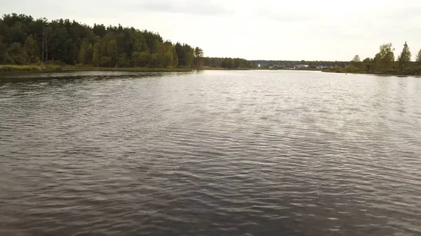 Water oppervlak met rimpelingen en zonnestralen reflectie met bewolkte lucht en bos op de achtergrond. Voorraadbeelden. Zomer rivier achtergrond met kleine golven van vuil water. — Stockfoto