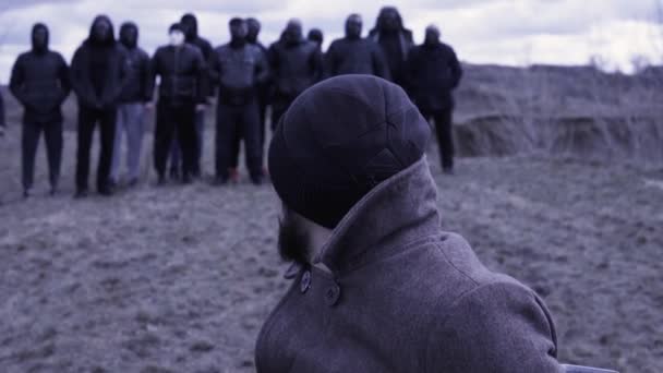 De man zit in een stoel en kijkt naar een groep gemaskerde criminelen. Beelden. Een ontmoetingsplaats voor gangsters. Groepering — Stockvideo