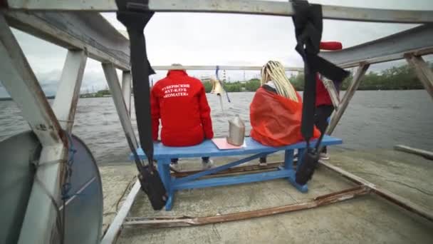 Moscú, Rusia-septiembre de 2019: Salvadores sentados en el muelle. Art. Vista trasera de dos socorristas sentados en el muelle con clima nublado. Dos rescatistas están esperando el final de la carrera de vela de mar — Vídeos de Stock