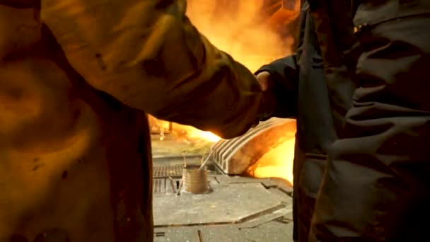 Visão traseira de duas siderúrgicas no lingote de fundição apertando as mãos na frente do forno de arco elétrico na loja quente, produção metalúrgica. Imagens de stock. Indústria pesada e conceito de acordo . — Vídeo de Stock