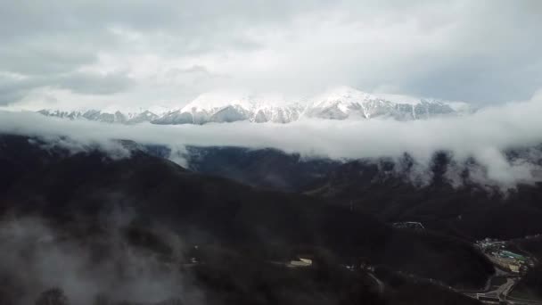 Flygfoto över det fantastiska vinterlandskapet i de snöiga sluttningarna och bergen i Alperna bland de frodiga vita molnen. Lagerbilder. Flyger över den gröna skogen och snöiga toppar i fjärran. — Stockvideo