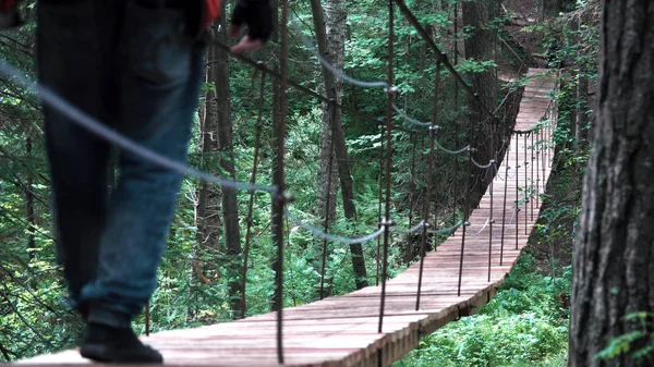 Man går på en hängbro i nationalparken, Usa. Lagerbilder. Bakifrån av en man vandrare med ryggsäck vandring i skogen med gångjärnsbro — Stockfoto