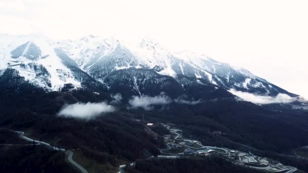 Herbst in nebligen Bergen mit Bäumen bedeckt und Skigebiet in ökologischem Gebiet. Archivmaterial. Antenne schöner bewaldeter Hügel und weißer schwerer Wolken in der Nähe von Gebäuden und Straßen. — Stockvideo