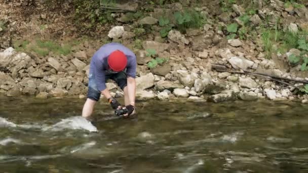 Hombre con una cámara de pie en un río rocoso y tomando fotos de la superficie del agua. Imágenes de archivo. Caminante masculino con una cámara filmando videos del arroyo del bosque . — Vídeo de stock