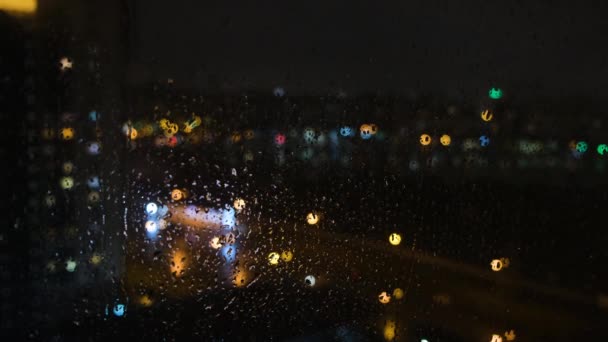 Raindrops on a window surface at night. Concept. Close-up of raindrops on the glass at night. Fluorescent lights outside the window at night — Stock Video