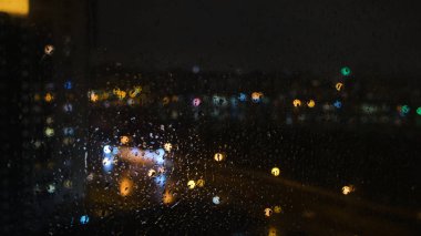 Geceleri pencere yüzeyine yağmur damlaları yağar. Kavram. Geceleri bardağa yağmur damlaları damlıyor. Geceleri pencerenin dışındaki floresan ışıkları...