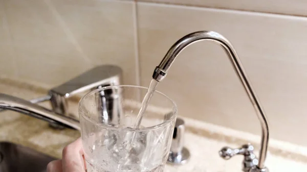 Woda wlewana do szklanki z kranu kuchennego. Koncepcja. Zbliżenie wody z kranu wlewanej do szklanki w kuchni — Zdjęcie stockowe