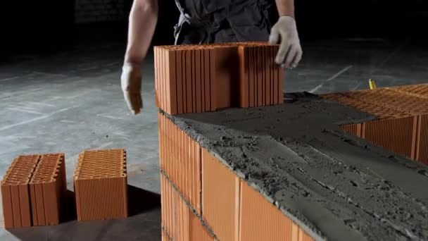 Bricklayer working at the construction site, making another layer of a brick wall. Stock footage. Bricklayer putting down red brick on cement basement. — Stock Video