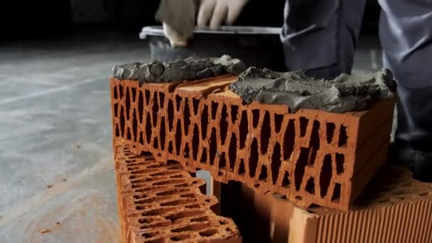 Κοντινό πλάνο ενός βιομηχανικού εργάτη που βάζει τσιμέντο στο τούβλο για κατασκευαστικές εργασίες. Στικ. Χέρια ενός ανθρώπου βάζοντας κονίαμα σε κόκκινο τούβλο, υλικά και κατασκευή έννοια. — Αρχείο Βίντεο