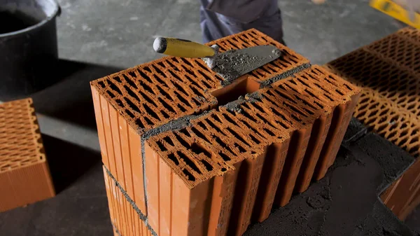 Bricklayer worker putting away extra cement with trowel putty knife on grey floor background. Stock footage. Man in gloves building a red brick wall.